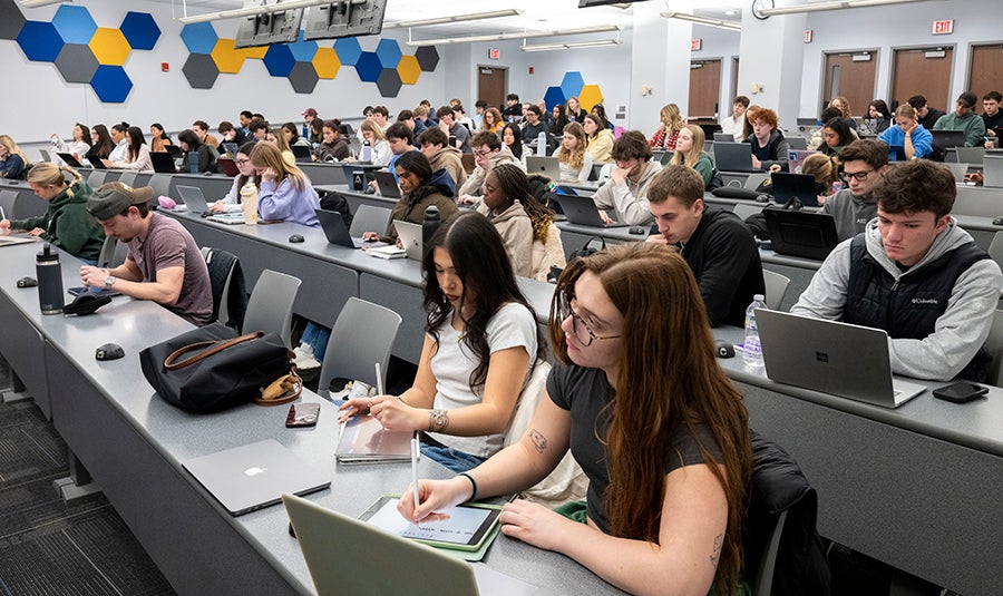 Large classroom of students taking notes during a lecture.