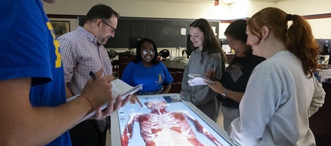 nursing students gather around an anatomage table showing bone and muscle structure during anatomy class.