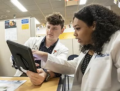 two health sciences students working in the Health Hub consult while looking at a tablet screen. 