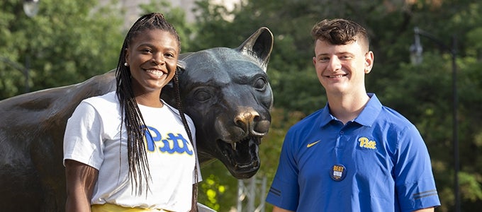 two students attending homecoming weekend posing with panther statue