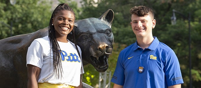 two students attending homecoming weekend posing with panther statue