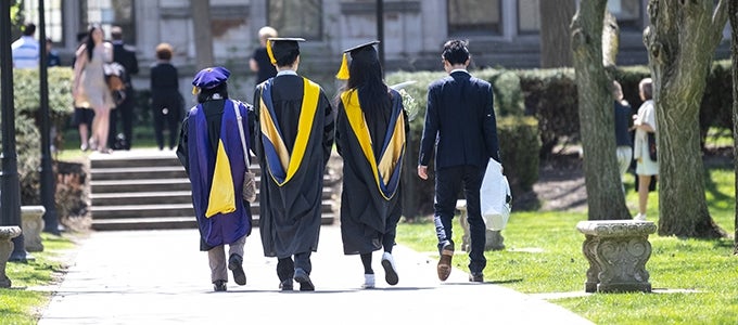 Pitt students in caps, gowns, and sashes walking on spring campus