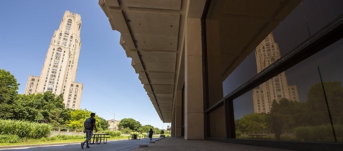 student walking past building with cathedral of learning in distance