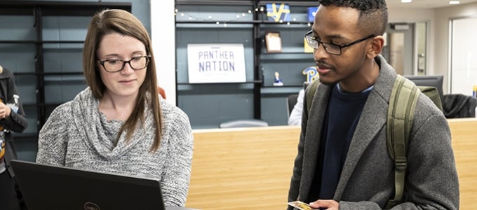 Student Success Hub staff member talke with student while showing them a computer screen.