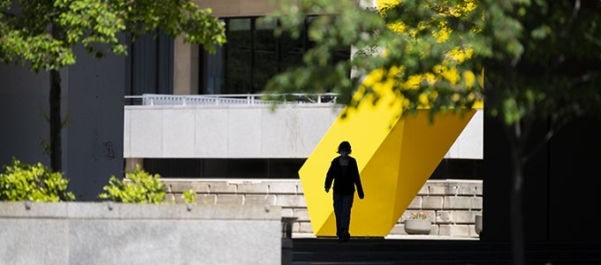 silhouette of student walking in front of yellow sculpture in Posvar Plaza on Pitt campus
