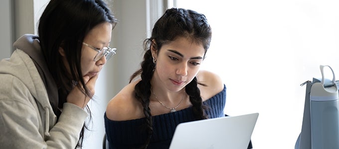 Two students look at a laptop screen together while working in the Writing Center.
