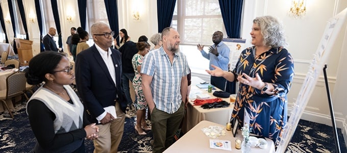 An awardee stands at a display table and describes her project to three attendees of the Year of Discourse and Dialogue capstone celebration.