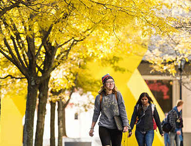 students walking on campus under yellow fall foliage